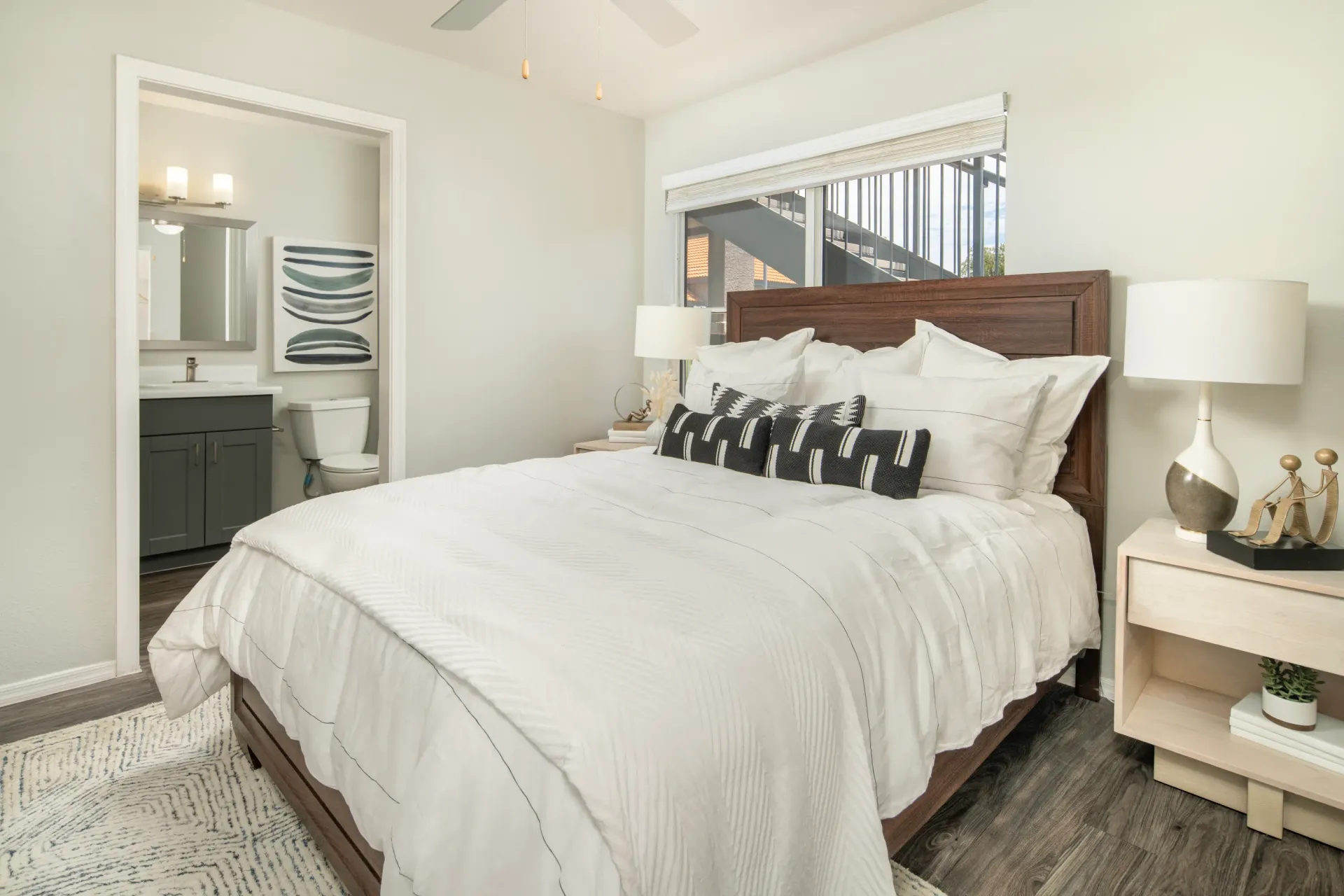 Cozy bedroom with a large white comforter, wood-framed bed, and a view into a modern bathroom at Sonoran Reserve in Tucson, AZ.