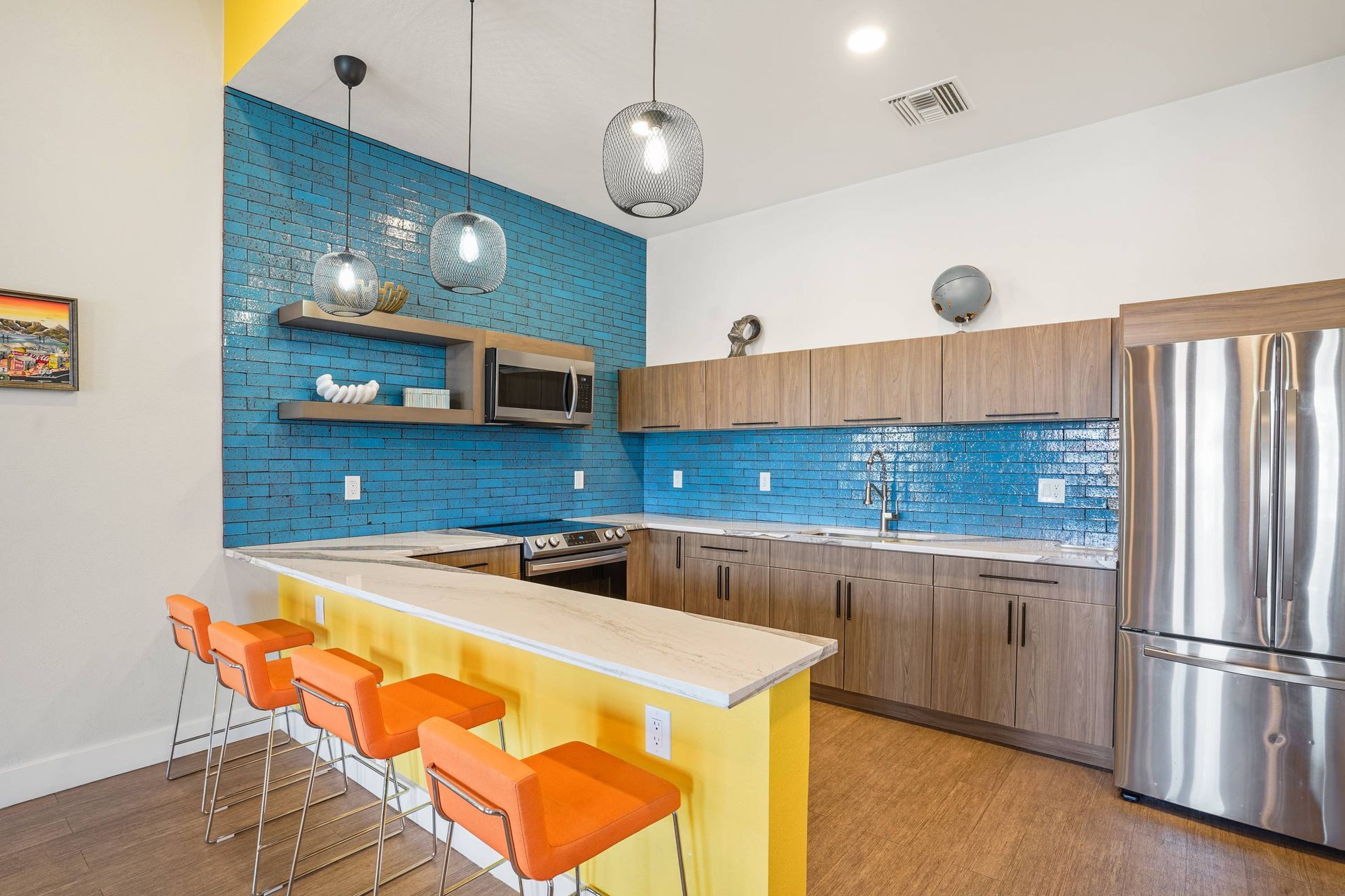 Modern apartment kitchen with blue tile backsplash, wood cabinets, stainless appliances, and a yellow breakfast bar. Schedule a tour today and discover why apartments for rent in Tucson, AZ like Sonoran Reserve offer comfort, style, and convenience in one welcoming community.
