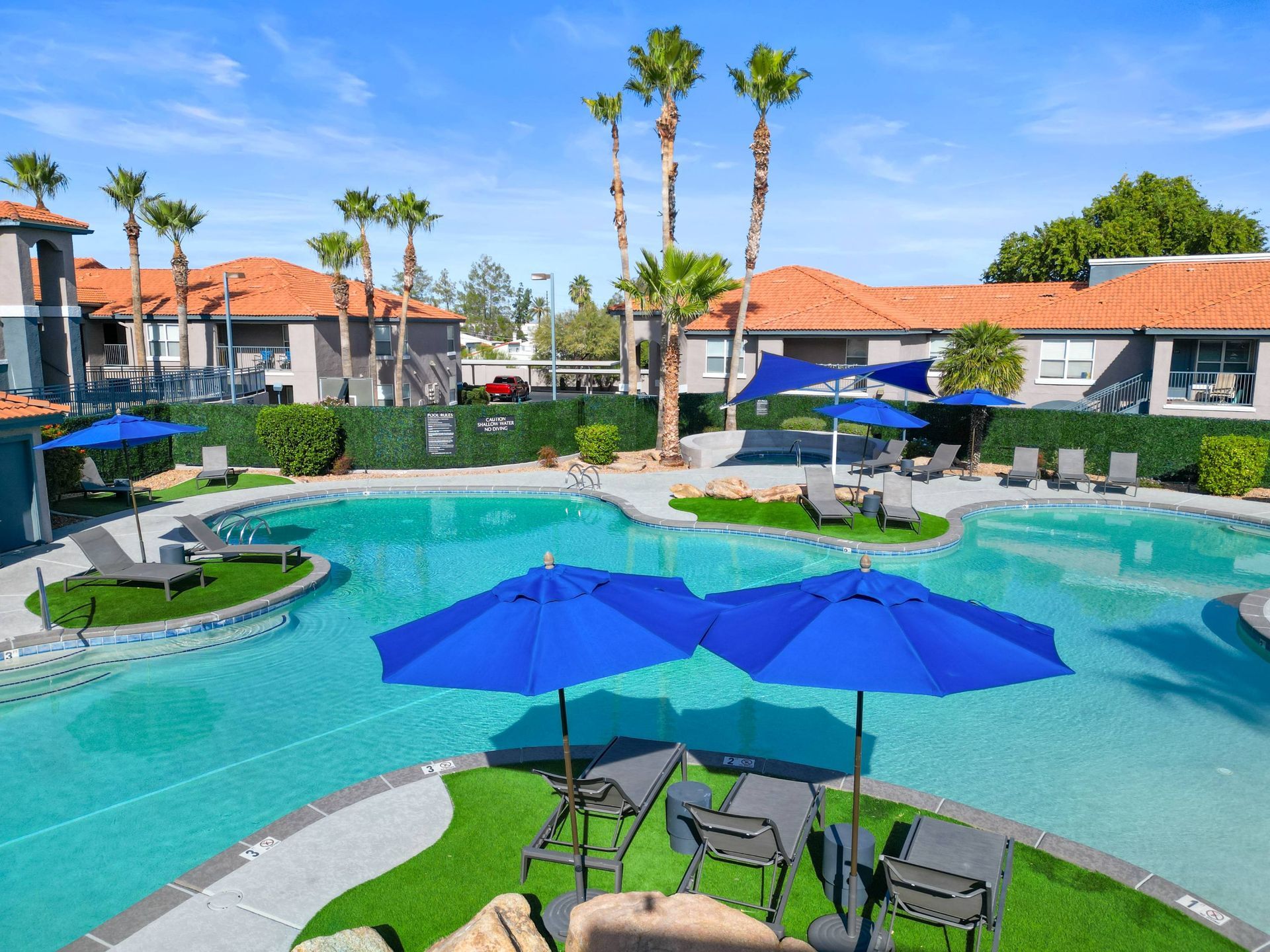 Outdoor pool area at a multifamily community with blue umbrellas, lounge chairs, and palm trees.  Take a tour of Sonoran Reserve and experience comfortable living in one of the most inviting apartments in Tucson, AZ.
