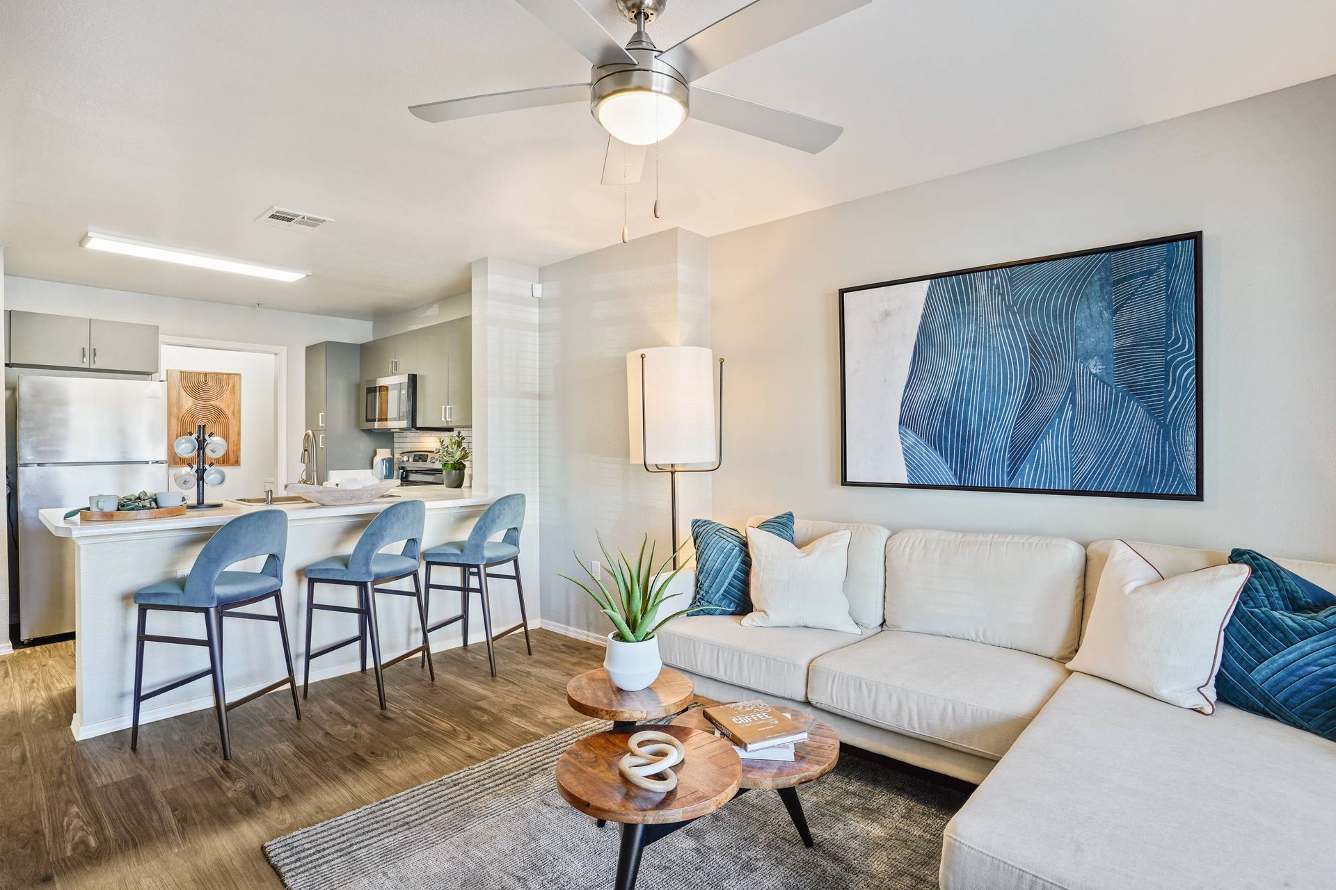 Open-concept living area with a kitchen island, blue bar stools, and a light sofa. Tour Sonoran Reserve to experience the space and comfort offered in our 4-bedroom apartments in Tucson, AZ.