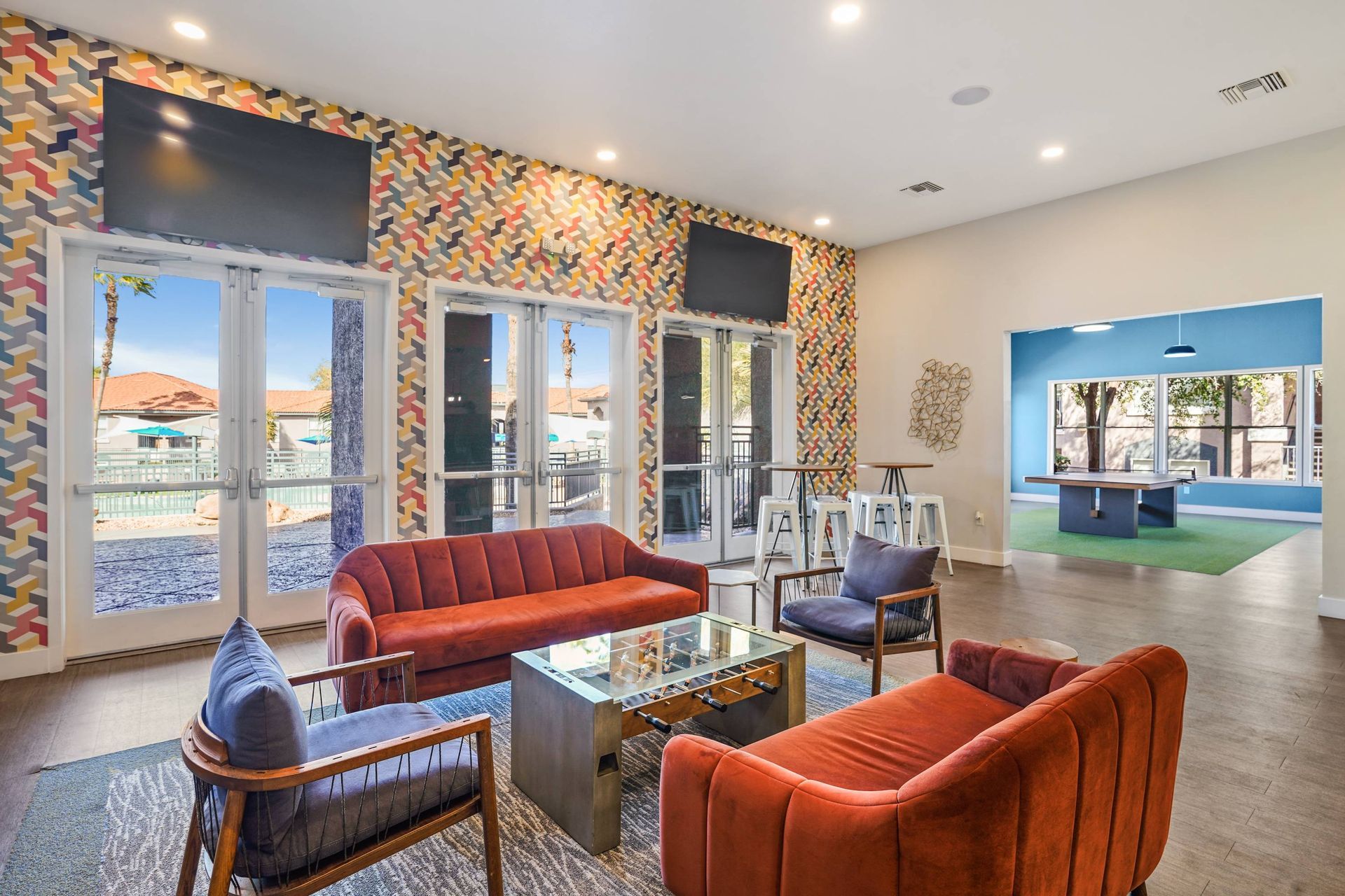 Communal lounge with colorful geometric wallpaper, glass exterior doors, wall-mounted TVs, and orange seating. Schedule a tour and see how our thoughtfully designed 2-bedroom apartments in Tucson, AZ offer the space and style you’ve been looking for.