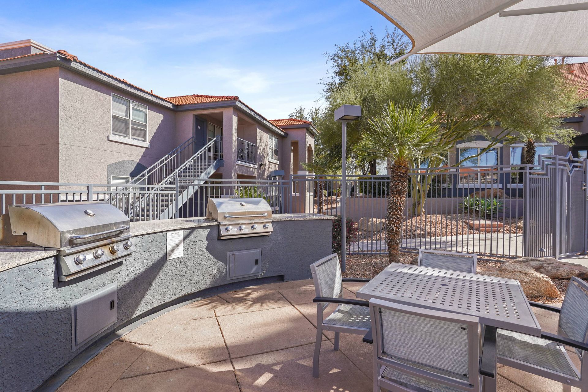 Outdoor communal grilling area with table, chairs, and palm trees in a gated apartment courtyard.  Come see why residents enjoy the lifestyle offered by our modern Tucson, AZ apartments at Sonoran Reserve.
