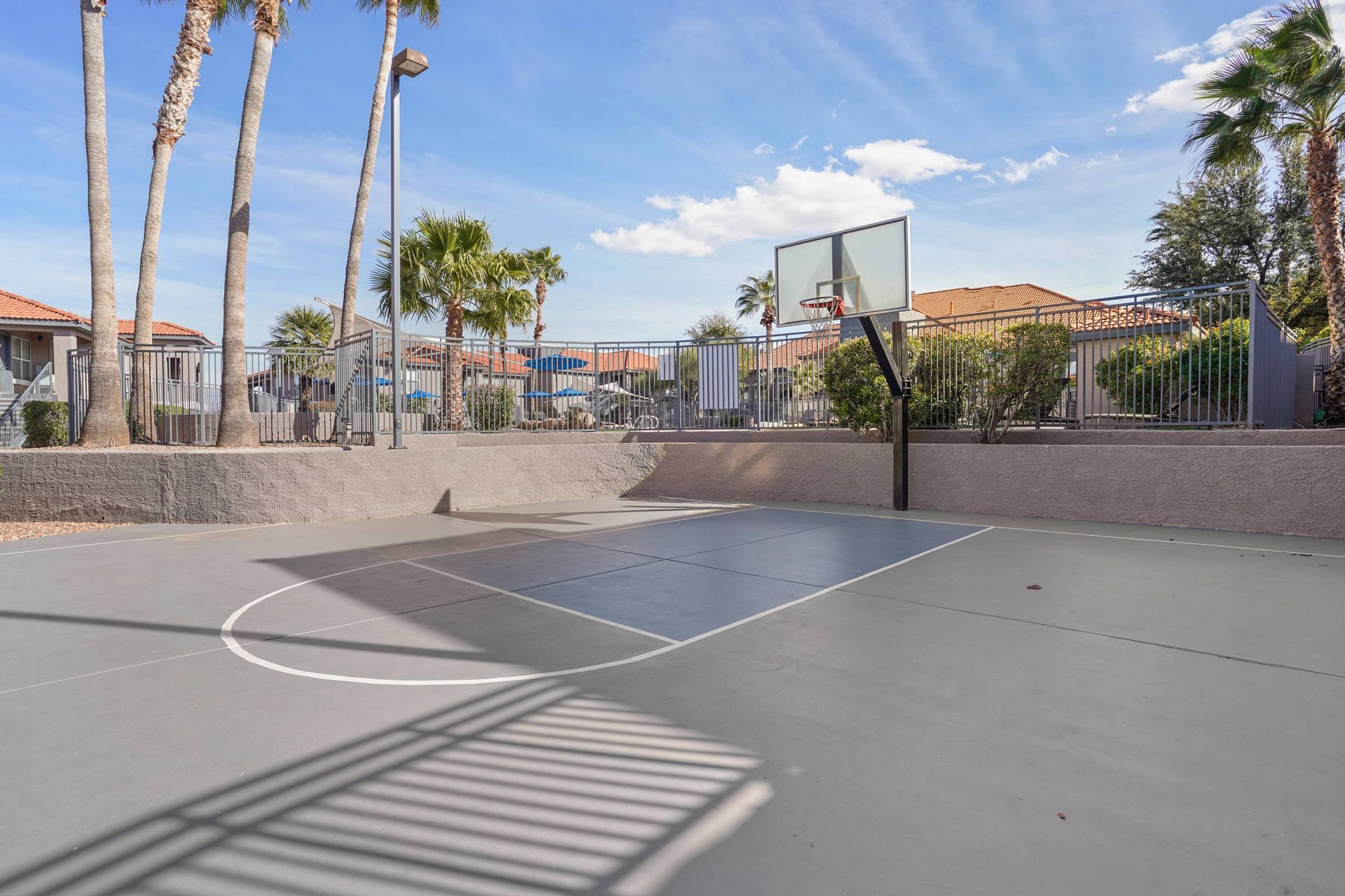 Outdoor basketball court with hoop, palm trees, and a surrounding fence.  Schedule a visit and explore thoughtfully designed rentals in Tucson, AZ at Sonoran Reserve.
