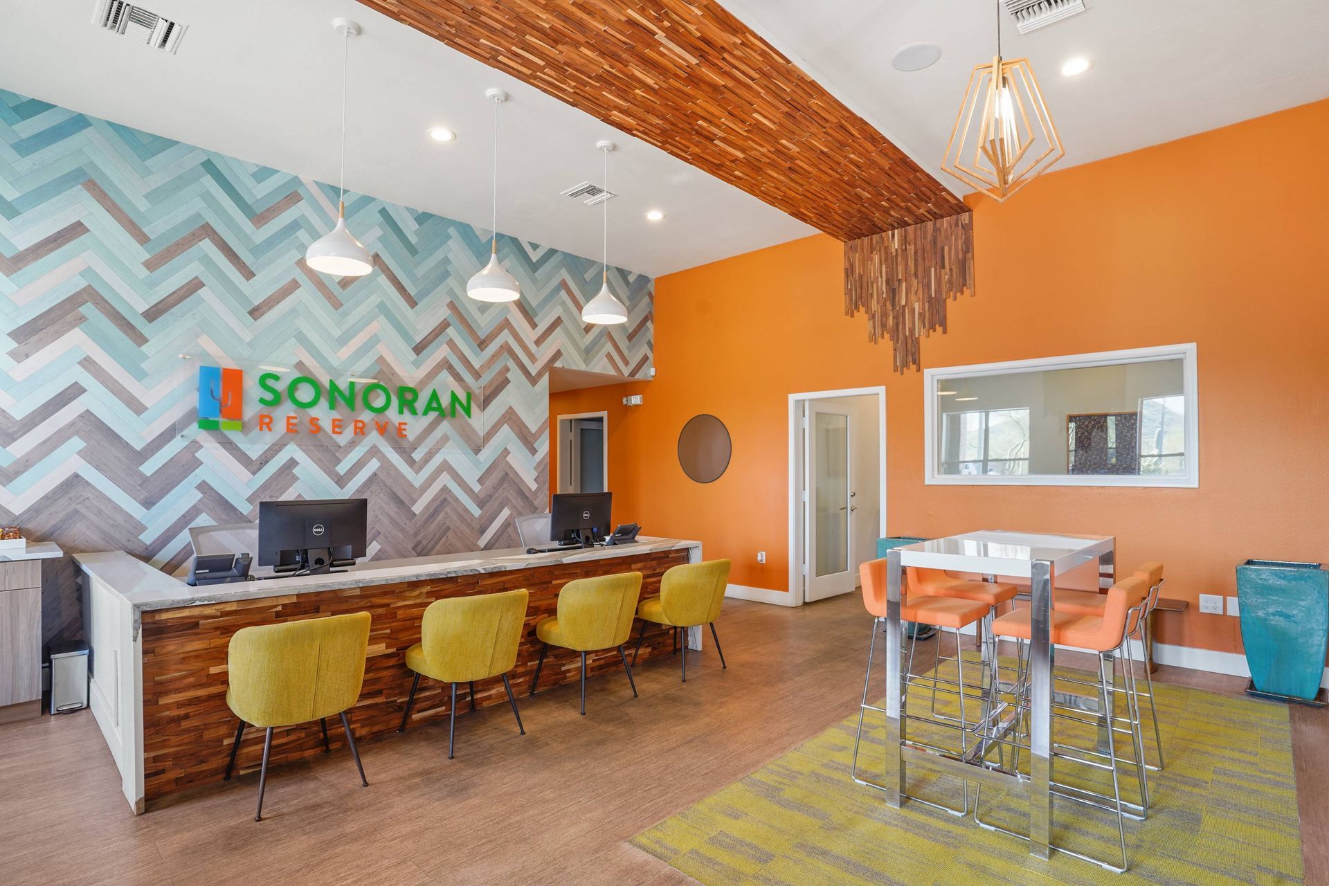 Leasing lobby with a long reception desk, chevron wall design, and orange accents.  Tour Sonoran Reserve today and explore spacious 1-bedroom apartments in Tucson, AZ, designed for comfort and convenience.
