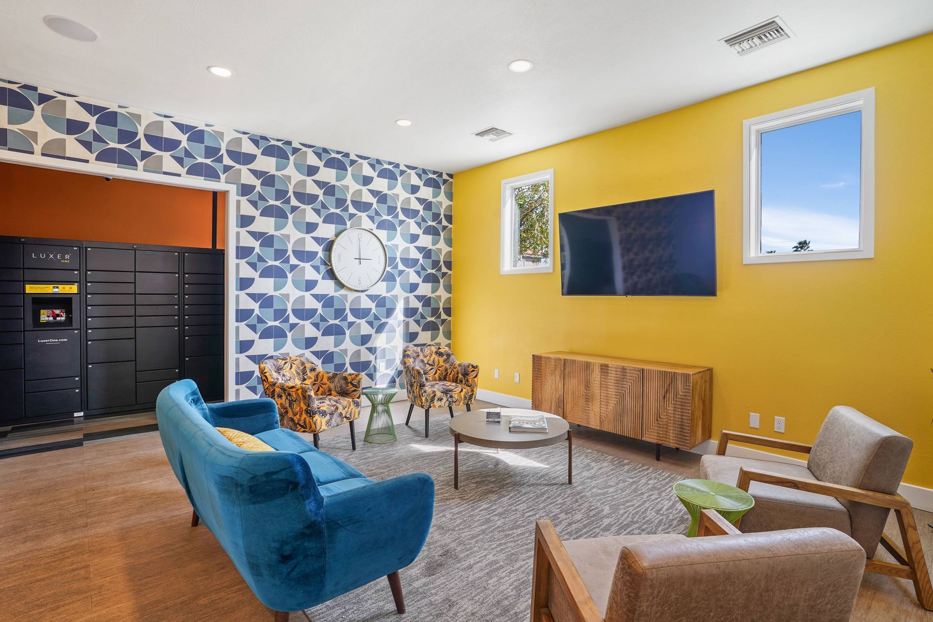 Modern communal lounge with blue geometric wallpaper, a yellow accent wall, and a wall-mounted TV.  We invite you to schedule a tour and explore beautifully designed apartments in Tucson, AZ at Sonoran Reserve.

