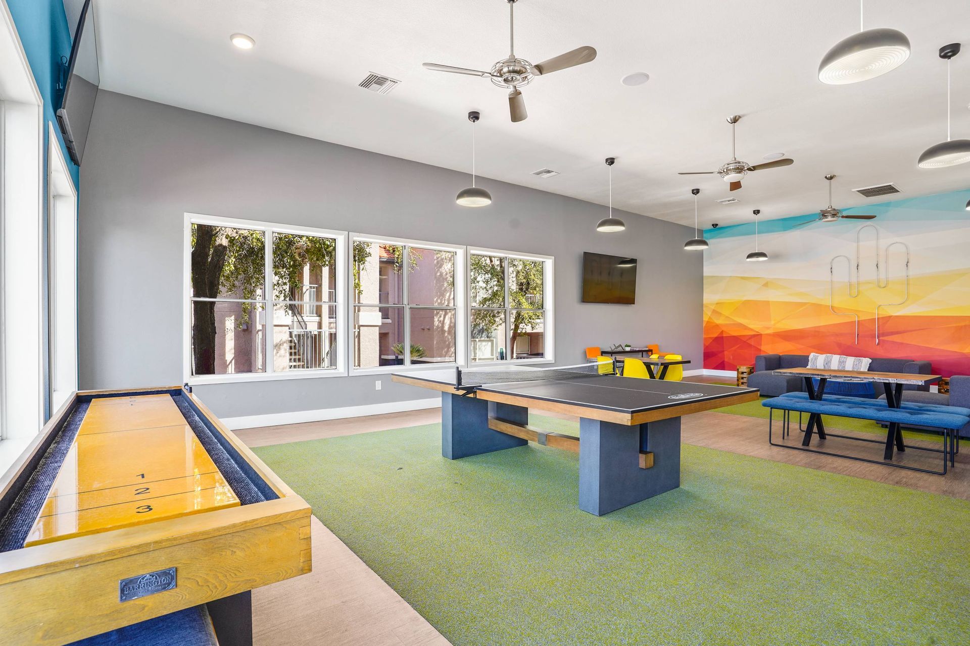 Bright indoor community lounge featuring a ping-pong table, seating, and a colorful mural.  Discover comfort and convenience by touring Sonoran Reserve, where quality rentals in Tucson, AZ, feel like home.
