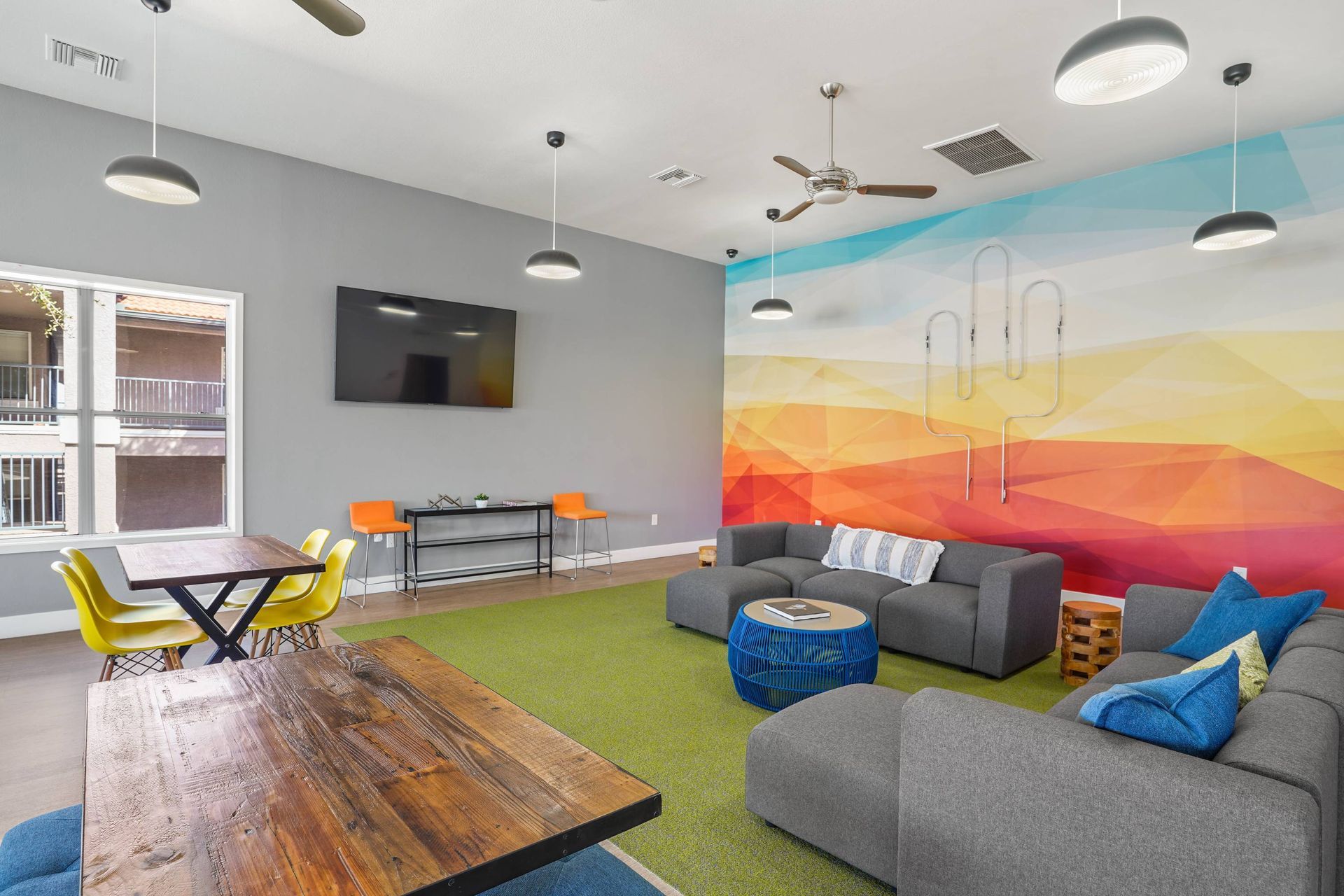 Modern resident lounge with gray sectional, colorful mural, and wall TV.  Visit Sonoran Reserve and see how our welcoming community stands out among Tucson, AZ rentals.
