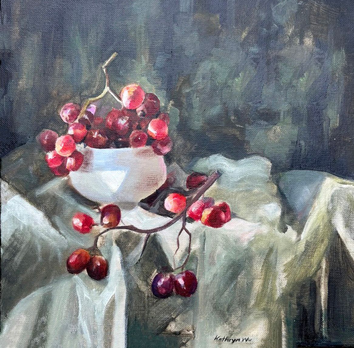 Still life of grapes in a white bowl and scattered on a draped tablecloth against a dark background