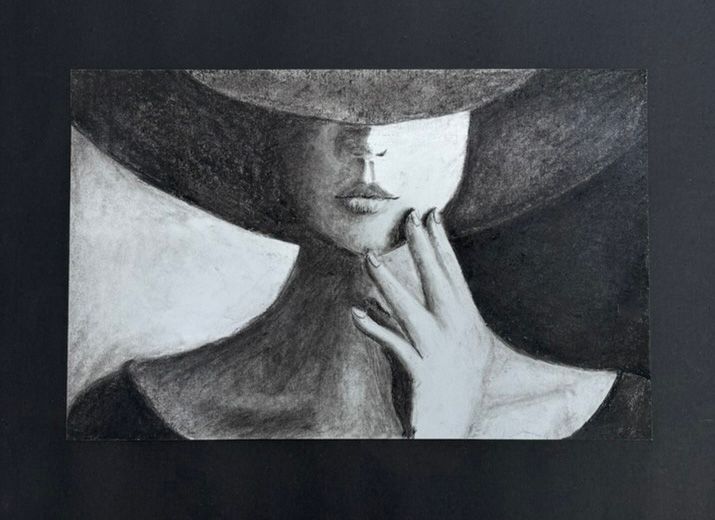 Black-and-white portrait of a face partly hidden by a wide-brimmed hat, hand touching the chin