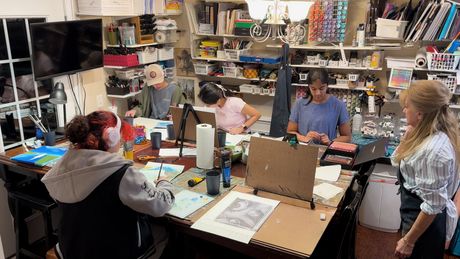 People gathered around a cluttered workshop table, working and talking in a busy studio.