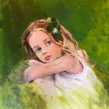 Portrait of a young girl with blonde hair and a green flower, resting her arms on a white surface.