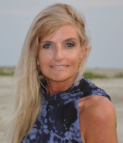 Portrait of a blonde woman in a blue patterned sleeveless top outdoors by the beach