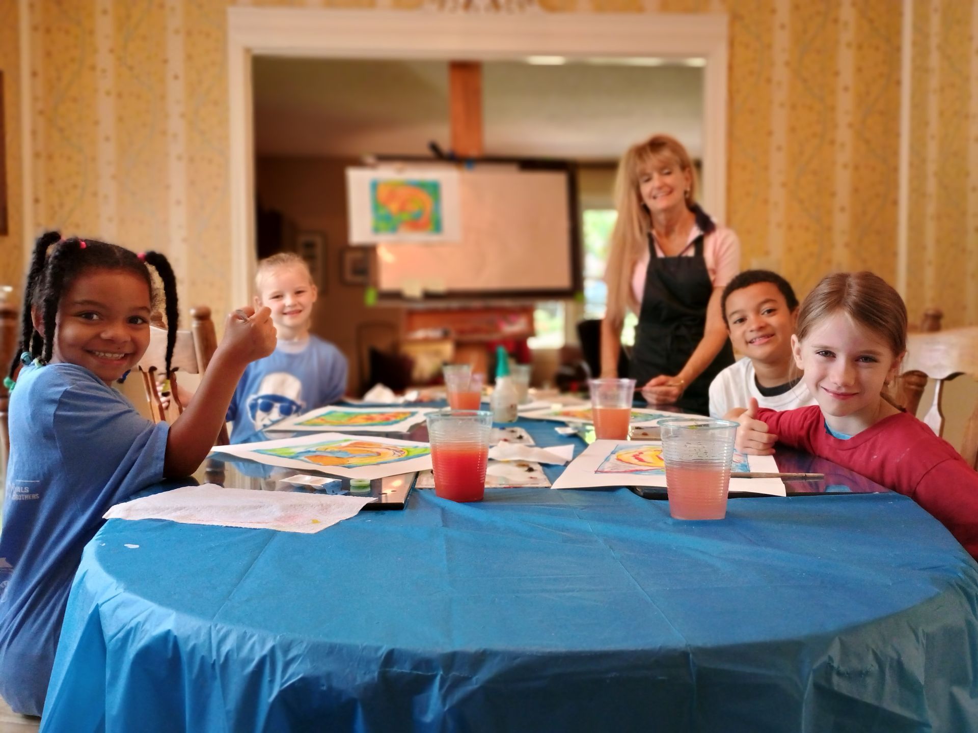 Children at a table in a classroom, smiling and waving during a group activity.