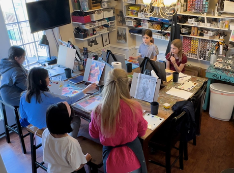 People gathered around a art table in a bright room, working with paints and supplies.