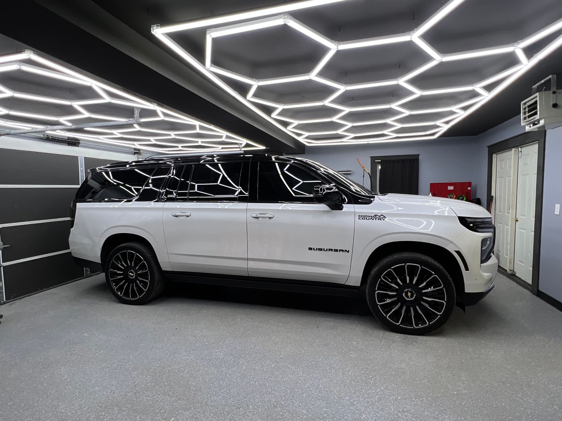 A white sports car is parked in a garage under a honeycomb ceiling.