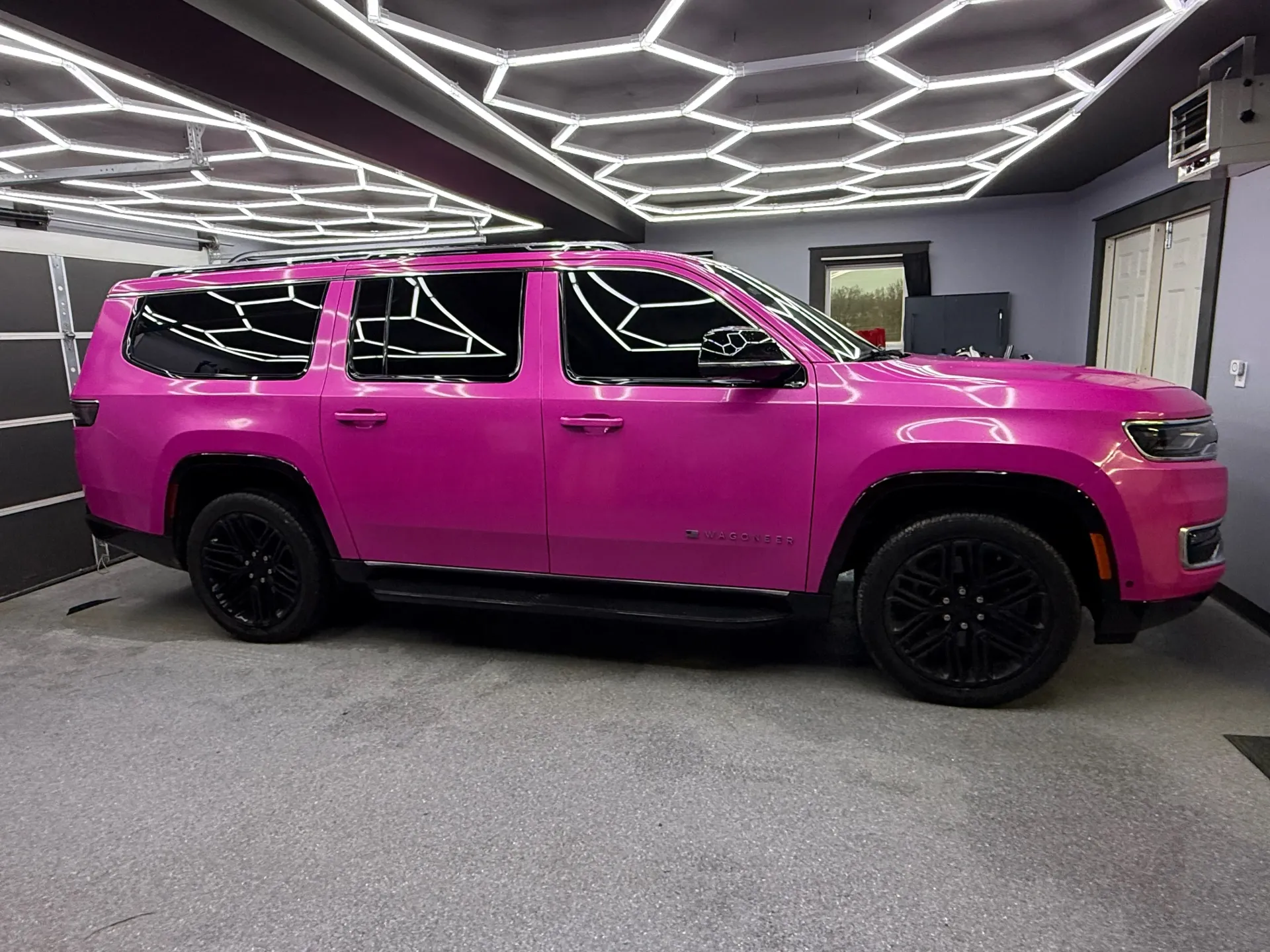 Bright pink SUV parked in a modern garage with hexagonal ceiling lights