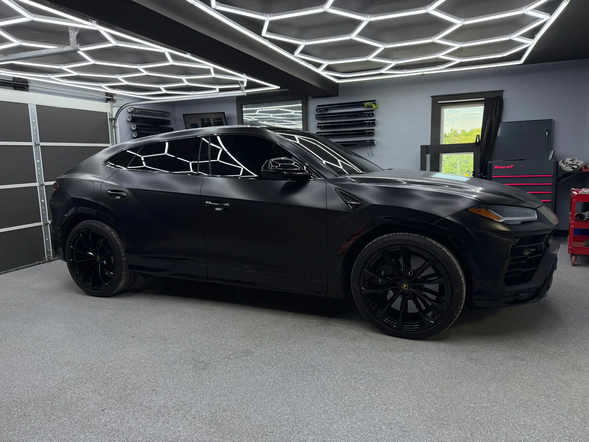 Black sports car in a modern showroom with geometric ceiling lights.