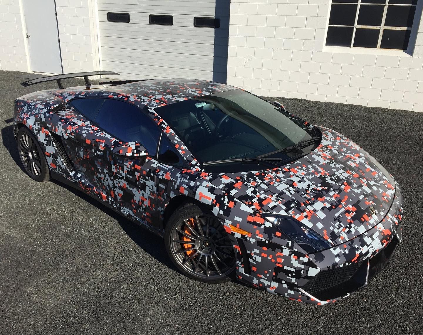 Lamborghini sports car with digital camouflage wrap parked in front of a building.