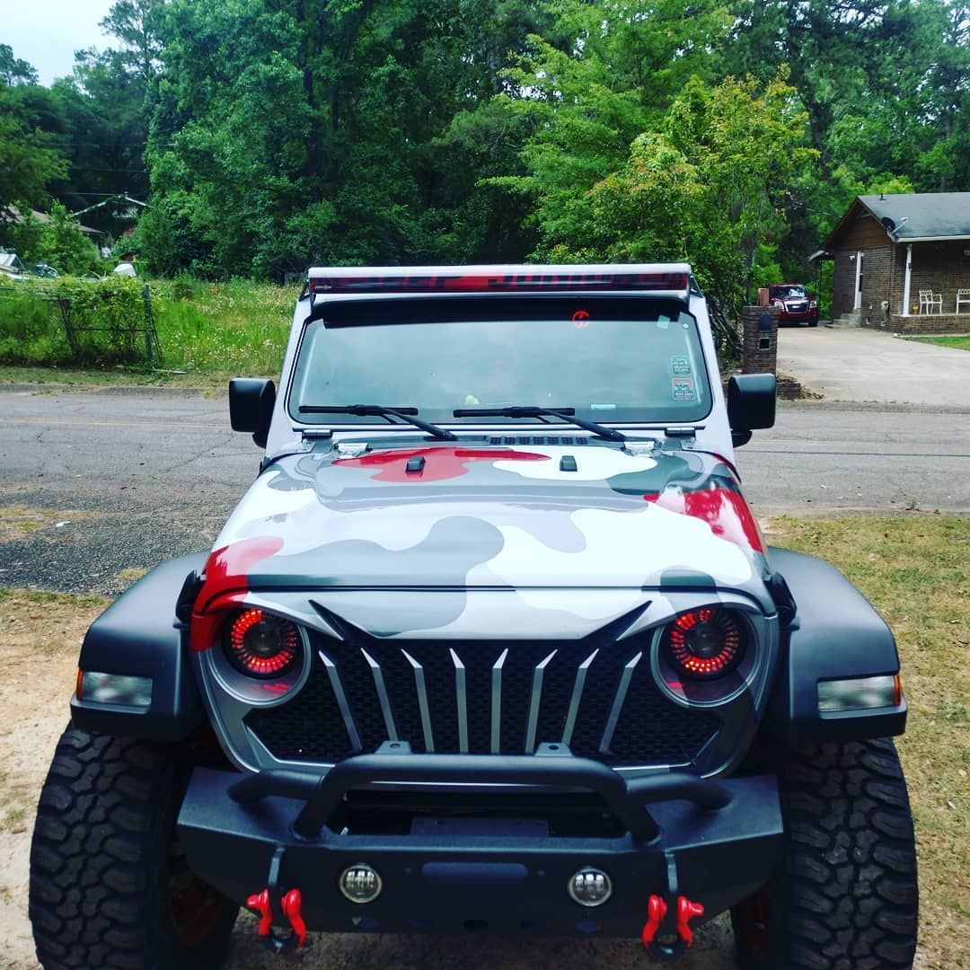 Customized camo Jeep with a front light bar, off-road bumper, and red accents parked outside.
