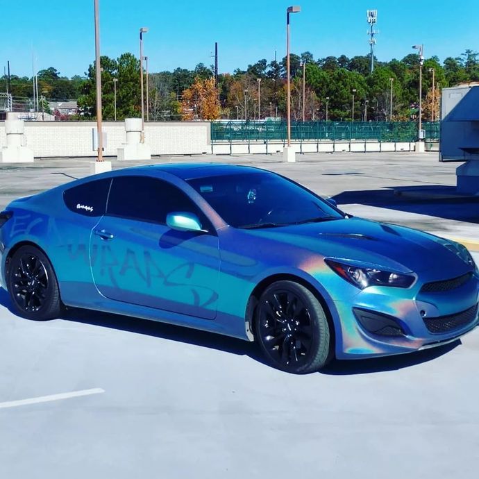 Blue iridescent coupe parked on a rooftop parking lot with black wheels.