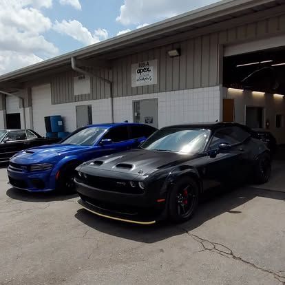 Two muscle cars, blue and black, parked outside a garage with 