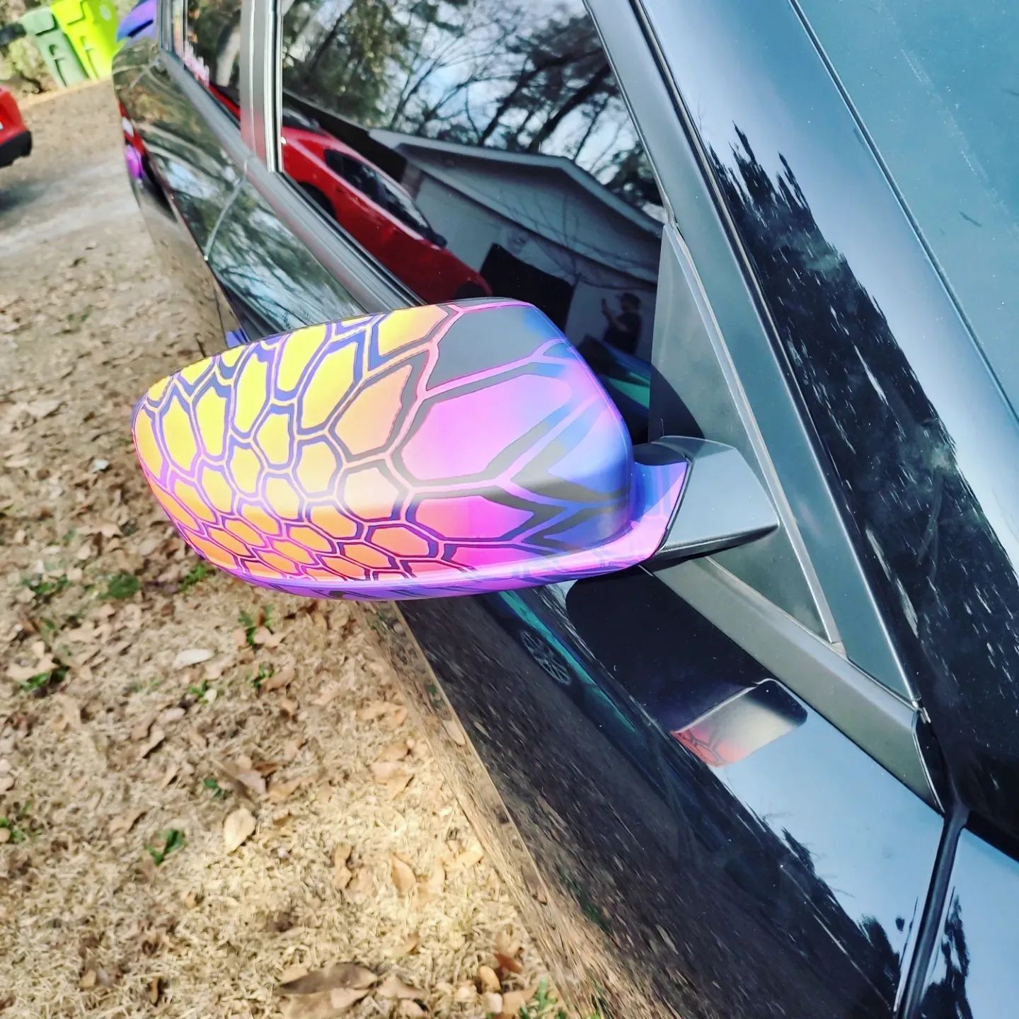 Black car with a side mirror in iridescent hexagonal pattern.