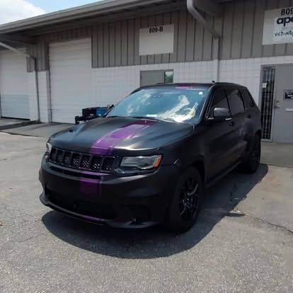 Black Jeep Grand Cherokee with purple stripes, parked outside a building.