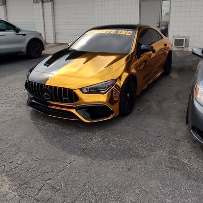 Gold and black Mercedes-Benz CLA car parked on asphalt. The car has a split color design and black wheels.