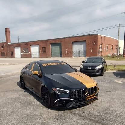 Black and gold car parked in front of a brick building. Another car is parked in the background.