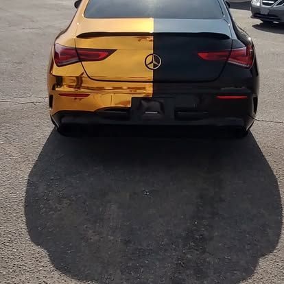 Rear view of a Mercedes-Benz car split gold and black, parked on pavement.