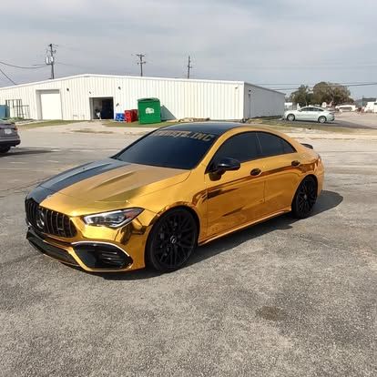 Gold Mercedes-Benz car with black accents parked on asphalt in front of a building on a sunny day.