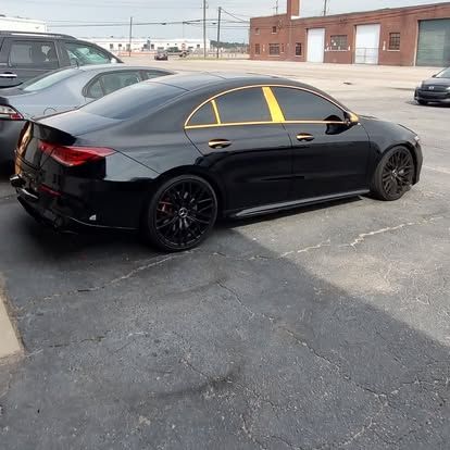 Black sedan with black rims and gold window trim parked on asphalt.