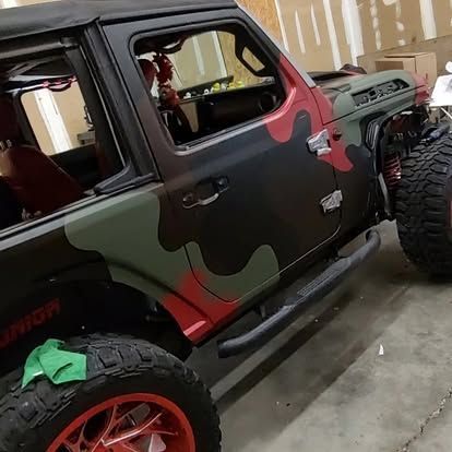 Camouflaged Jeep with red accents and large tires parked indoors.