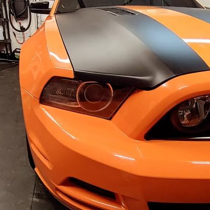 Orange Ford Mustang with black hood stripe, tinted headlights.