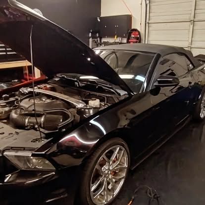 Black Ford Mustang convertible with hood open in a garage, engine exposed.