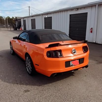 Orange convertible Mustang with a black top parked in front of white storage units.