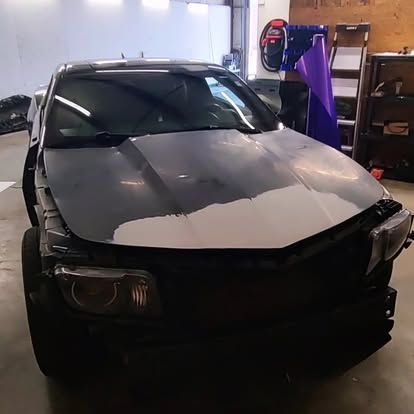 Black car hood with patches of primer, in a garage.