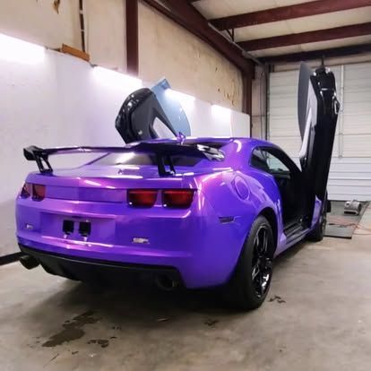 Purple sports car with gullwing doors open in a garage.