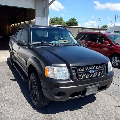 Black Ford Explorer Sport Trac pickup truck parked in front of a garage on a sunny day.
