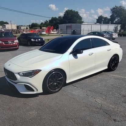 White Mercedes-Benz CLA with a black roof and black rims parked on asphalt on a sunny day.