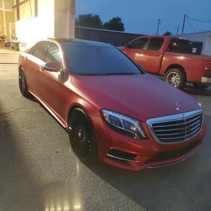 Red Mercedes sedan parked next to a red pickup truck, both in an outdoor setting.