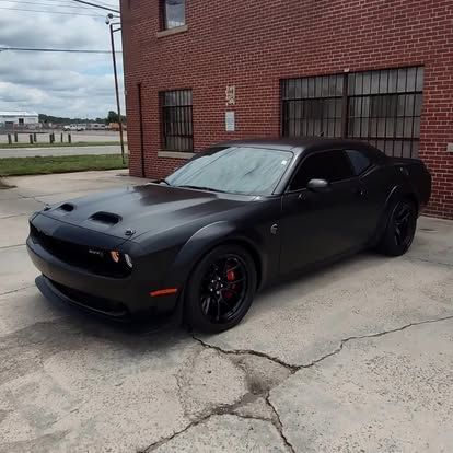 Black Dodge Challenger parked in front of a brick building.