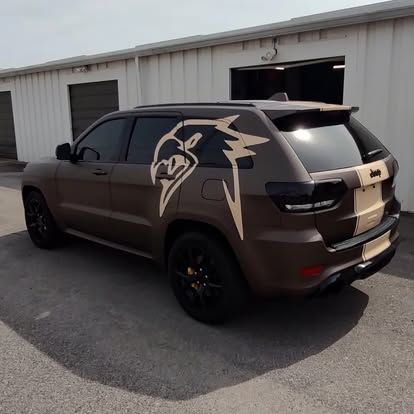 Brown Jeep Grand Cherokee with tan snake graphic and racing stripe, parked outside a building.