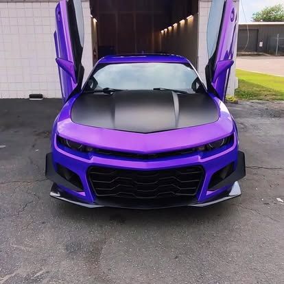 Purple car with open gullwing doors, black hood, and front spoiler, parked.