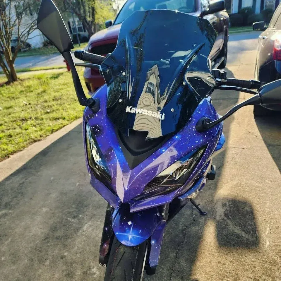 Blue Kawasaki motorcycle with galaxy-themed paint, parked outside on a sunny day.