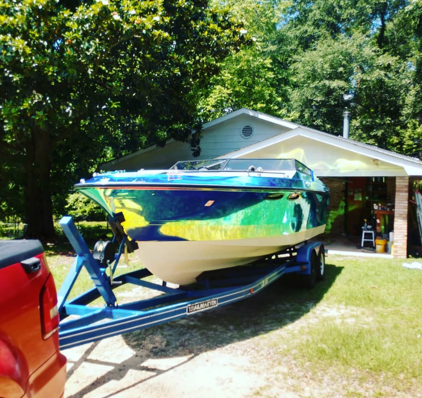 Blue and green speedboat on a trailer in front of a house.