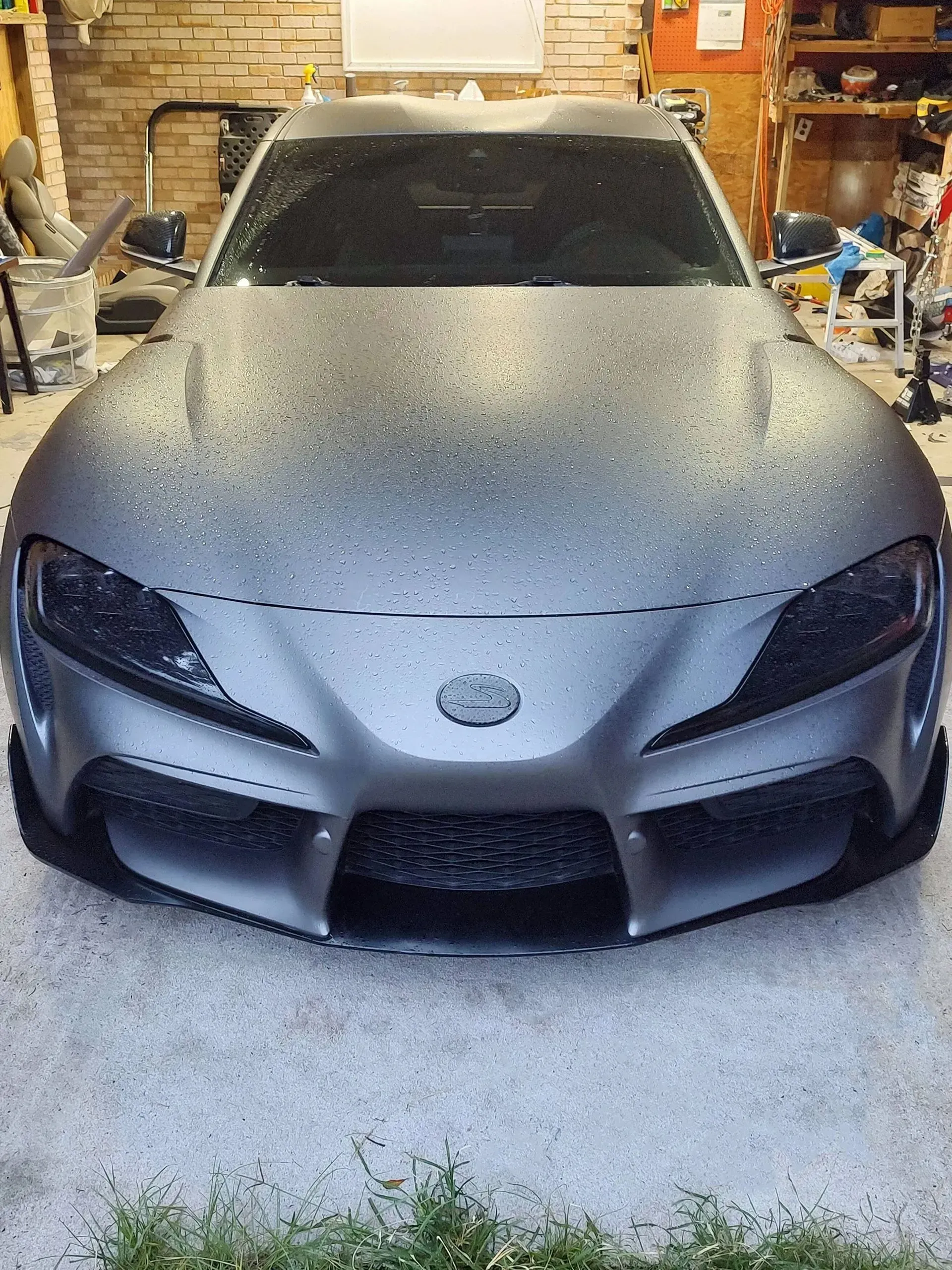 Gray Toyota Supra sports car in a garage, covered in water droplets.