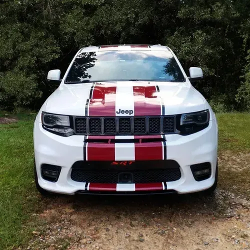 White Jeep Grand Cherokee SRT with red racing stripes, parked in front of trees.