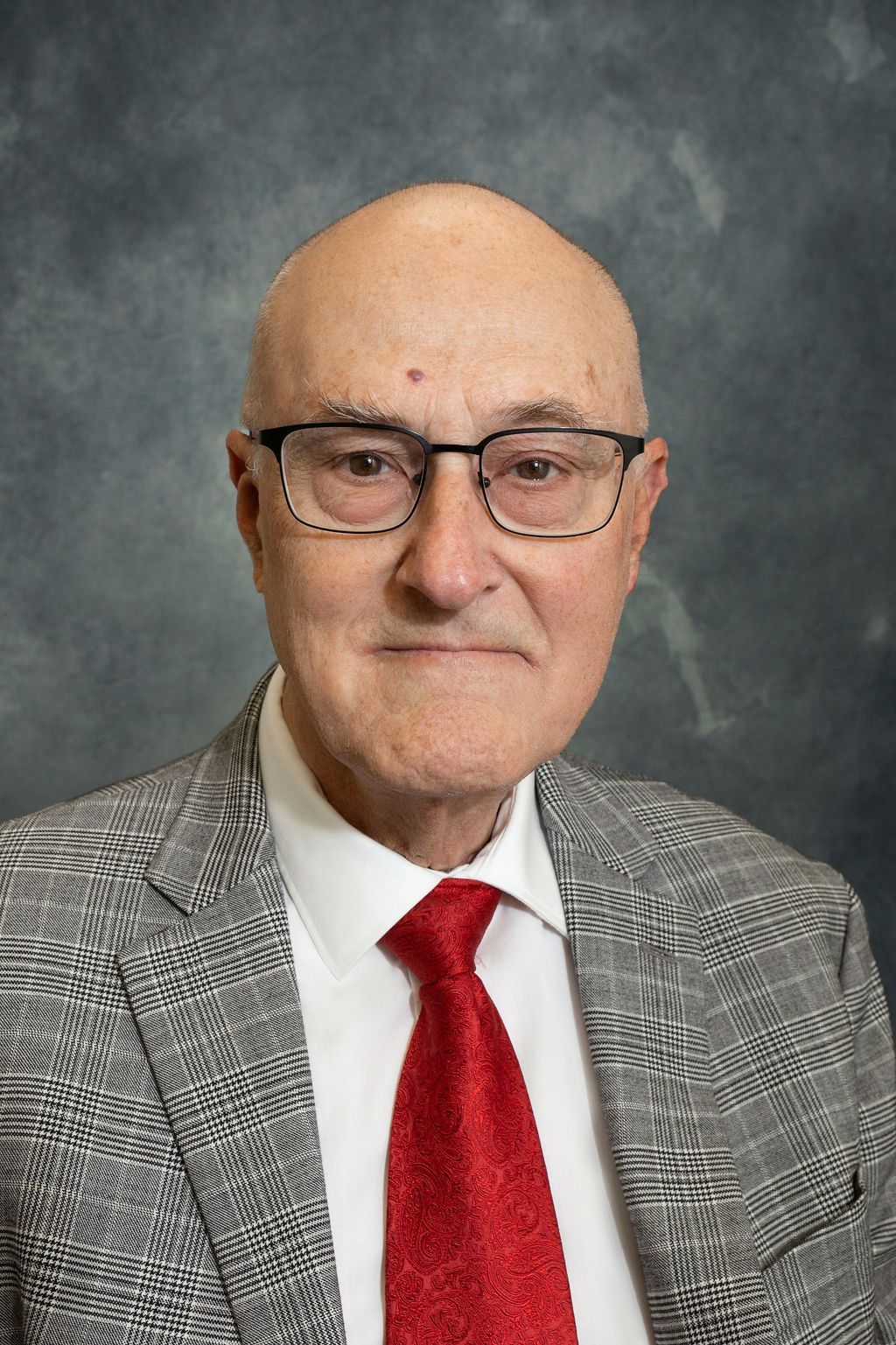 A bald man wearing glasses , a suit and a red tie.