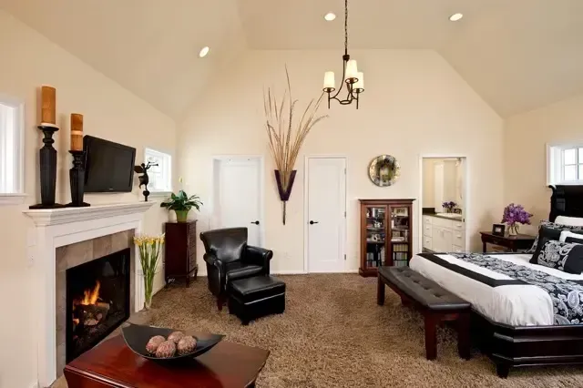 Bright living room with fireplace, chandelier, black leather chairs, and a dark wood bed in the corner